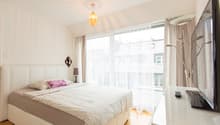 white bed, white bedhead, white pillow, brown blanket, lamp, tv, wooden floor