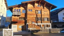 Large wooden house with several floors, wooden balcony, and a staircase leading to the entrance.