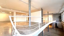 Empty room with concrete floor, white railing on the second floor, several pillars, lamps on the ceiling