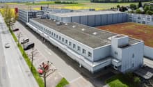 Large industrial building, white paint, flat roof, windows, parking spaces, road