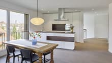 Modern kitchen with dining area, large windows, wooden floor, table and chairs, hanging lamp, stainless steel range hood, flowers in vase