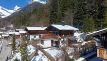 chalet style house, wooden exterior, snow covered roof, balcony, surrounded by trees and mountains