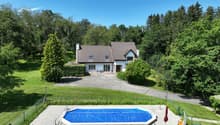 House with brown roof, white walls, swimming pool, driveway, fenced area, green landscape