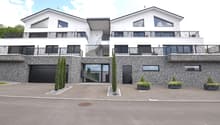 2 story modern house, white and grey exterior, two garages, balconies on each floor, planted area in front