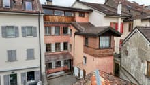Multiple buildings with balconies, brick and wood construction, various window sizes, red shutters