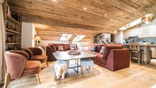 room features wooden ceiling and hardwood floors, couch with pillows, table, chairs, kitchen and dining area visible in the background