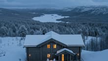 Wooden log cabin in a snowy mountainous landscape with a view of a lake