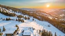 Three buildings set in a snowy mountainous region, surrounded by pine trees and ski trails