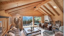 Living room with wooden walls, large windows, fireplace, glass table, couches, armchairs, and decorative items