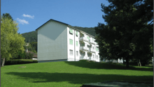 3-story apartment building with green exterior, surrounded by a grassy lawn and trees