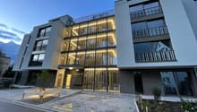 Contemporary apartment building with 4 floors, balconies, grey walls, and illuminated signage, private parking.