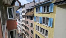 An aerial view of several buildings with various colors and blue shutters. The building in the center has a balcony with a metal railing.