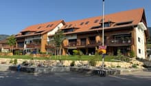 Apartment building with brown roof, balconies, large windows, stone wall, and trees in front