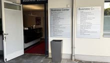 Entrance to a business center with an open door, a red carpet, a trash bin, and a signboard with the text 'Business Center'.