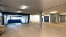 large open space, concrete floor, metal beams, large blue doors, storage boxes, stacks of wooden pallets