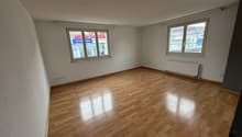Spacious room with hardwood flooring, large windows, and a radiator. The room appears to be empty, ready for furnishing and occupancy.