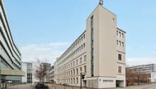 White exterior, multiple floors, rectangular windows, two entrances with text 'dreamtime', antennas on the roof, trees and bicycle stands in front, buildings behind the main building