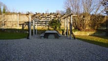 wooden pergola, concrete table, gravel surface, wooden fence