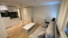 open floor plan, gray couch, white coffee table, kitchen, white cupboards, hardwood floor