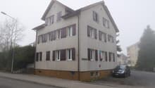 Gray apartment building with multiple windows, brown base, streetlight and parking in front