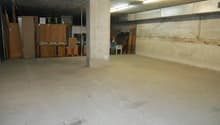 Large open basement space with concrete floor, exposed ceiling, and storage boxes and furniture items along the walls.