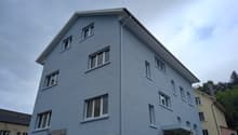 Large blue apartment building with windows, roof gutter, gray foundation, sign reading 'Nur für Berechtigte' on the left side