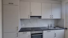 Modern kitchen with white cabinets, marble-patterned backsplash, black countertop, built-in oven, and a dishwasher