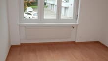 Empty room with wooden floors, large window, heater