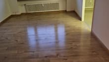 Empty room with white walls, white ceiling, wooden floor, large window with white shutters, white radiator