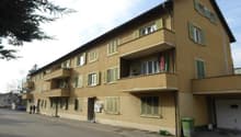 3-story apartment building, beige wall, green windows, multiple balconies, garage at the entrance