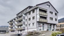 Multi-storey building with multiple balconies and windows, car parking area in front