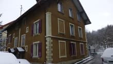 2 story house, brown exterior, white windows, purple shutters, chimney, front yard with snow, 3 cars parked in front