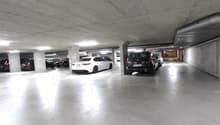 underground parking lot with concrete walls and columns, fluorescent lighting, multiple vehicles parked