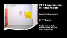 The image shows a storage room or warehouse space. The room has white walls, a red door, and signage on the wall indicating that there are 217 storage spaces available in Regensdorf. The signage also mentions that there is 24/7 access and that all additio