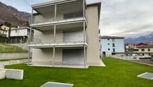 3-story modern apartment building with balconies, garage, and grassy lawn area in front