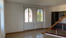 Spacious living room with large arched windows, hardwood floors, and a modern kitchen area with black cabinets.