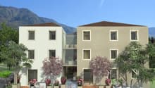 2 story building, beige exterior, glass entrance, balcony on the second floor, greenery surrounding