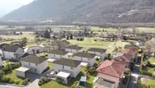 Cluster of modern houses, each with a garage, set in a green landscape with a mountain in the background