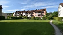 Apartment building with brown roofs, several floors, balconies, located in a green area with a large lawn