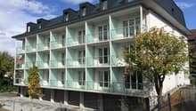 3-story apartment building with white exterior, glass balconies, and black roof dormers