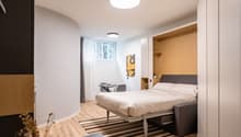 Spacious bedroom with hardwood flooring, white walls, large window, modern bed frame, built-in wardrobe, and a desk area
