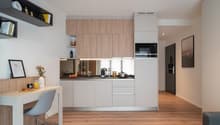 Modern kitchen with light wood cabinets, white appliances including a dishwasher, and a small dining area with a table and chair