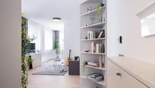 Spacious living room with white walls, hardwood floors, large windows, built-in shelving unit, potted plants, guitar, and a couch