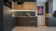 Modern kitchen with dark cabinets, wooden accents, stainless steel appliances, and a colorful abstract artwork on the wall