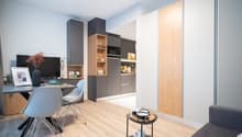 Modern kitchen with gray cabinets, wooden shelves, and built-in appliances including a dishwasher. Open concept living space with dining area and hardwood floors.