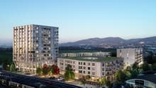 Two high-rise buildings, parking area, green grass, street with tram and cars, trees, green roof on one building, mountains in the distance.