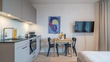 Open plan kitchen with a sink, gas stove, cabinets, microwave, and a dining table with chairs. Next to it is a bedroom with a bed.