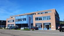 Two-story building with blue and brown exterior, multiple windows, and a parking area in front.