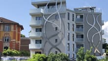Building with modern architecture, large windows, multiple floors, white and gray facade, balconies on multiple levels, metal railings on balconies.