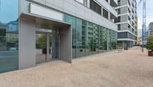 Modern office building, glass facade, entrance with glass doors, brick pavement, central location, nearby construction